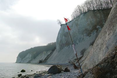 Flag by chalk cliff at beach against sky