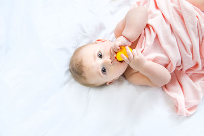 Portrait of cute baby girl holding rubber duck lying on bed