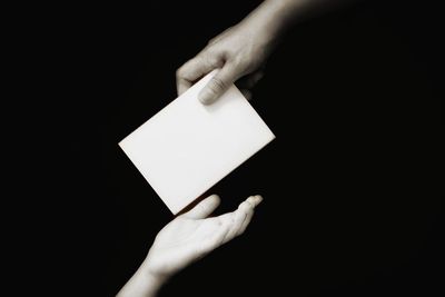 Close-up of hand holding paper against black background
