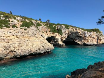 Rock formations in sea against clear blue sky