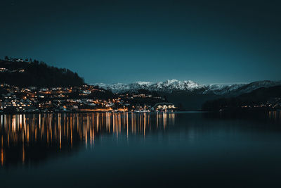 Scenic view of lake by mountains against clear sky at dusk