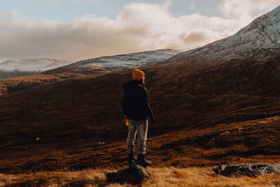 Man staning in golden plain looking at snow-capped mountains on highland hike in scotland.