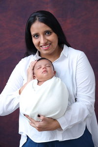 Portrait of smiling young woman with her new born baby wrap in white swaddle blanket