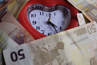 Close-up of heart shape alarm clock amidst european union currencies
