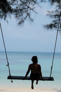 Rear view of woman sitting on sea against sky