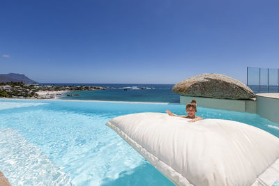 Man relaxing in swimming pool against clear blue sky