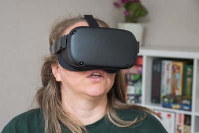 Close-up of a girl in vr glasses against a gray wall and a rack of games. the woman travels through