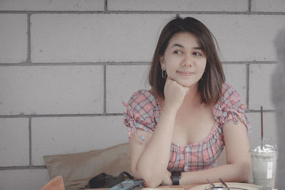 Portrait of a young woman sitting against wall