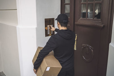 Rear view of delivery man ringing bell at doorstep