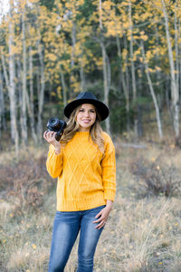 Full length portrait of a smiling young woman holding a camera