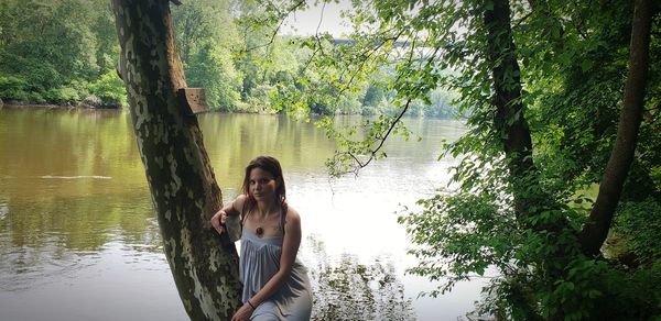 Portrait of young woman sitting on tree trunk against lake