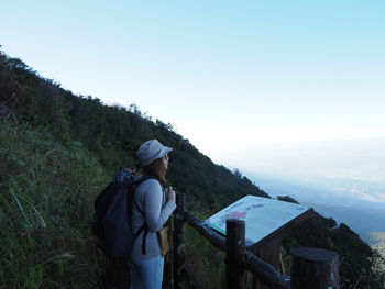 Side view of woman standing by information sign against landscape