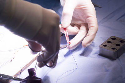 Cropped hands of doctor cutting stitches over table