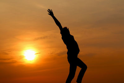 Low angle view of man with arms raised standing against orange sky