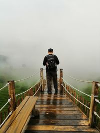 Rear view of man standing on footbridge amidst fog