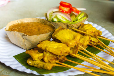 Pork satay grill on a paper dish served with ingredients slice chili, slice cucumber and spicy sauce