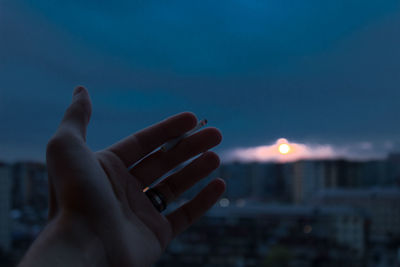 Close-up of hand holding cigarette against sky at night