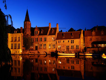 Illuminated buildings by river against clear sky at night