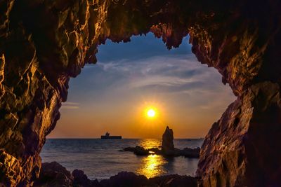 Scenic view of sea seen through cave against sky during sunset