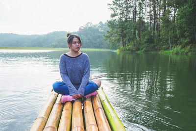 Full length of woman sitting on wooden raft in lake