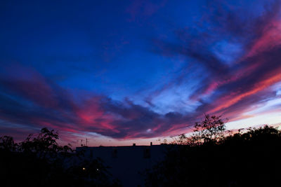 Silhouette trees against dramatic sky during sunset