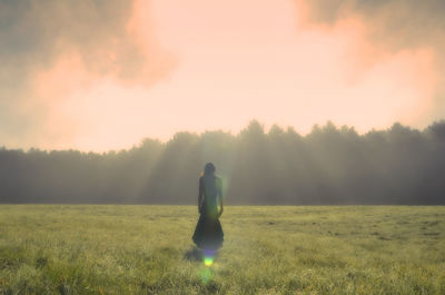 Rear view of woman standing on field against sky