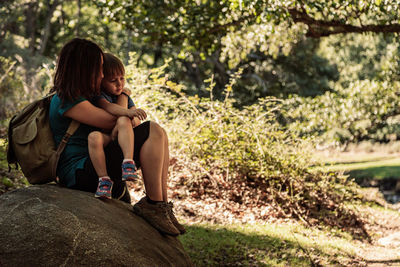 Rear view of women sitting on rock against trees