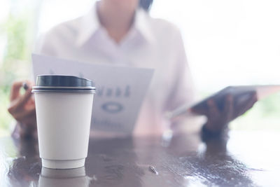 Close-up of disposable cup with woman in background