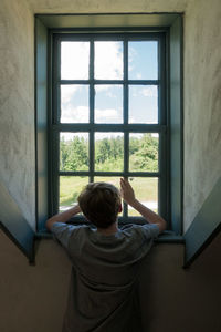 Rear view of boy looking through window at home