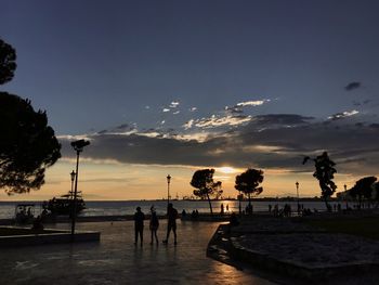 Silhouette people on beach against sky during sunset