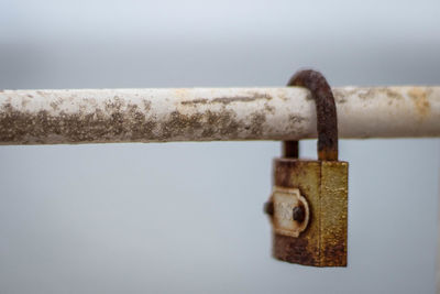 Close-up of rusty padlock hanging on railing against sky