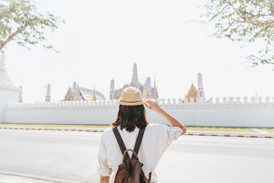 Rear view of woman standing by road against sky in city