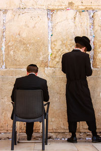 Rear view of two men sitting against wall