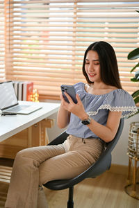 Young woman using mobile phone while sitting on sofa at home