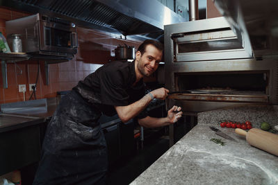 Handsome pizzaiolo making pizza at kitchen in pizzeria.