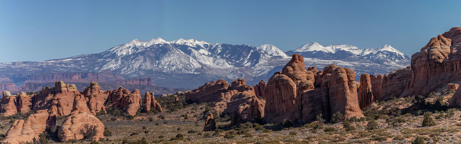 Panoramic view of sandstone rock formations against snow capped mountains on a sunny day