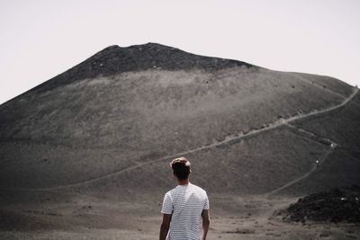 Rear view of mid adult man looking at mountain against clear sky