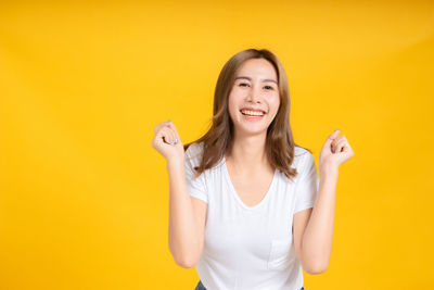 Portrait of smiling young woman against yellow background