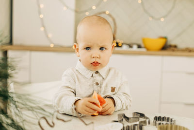 A sad kid with a grapefruit in his hands is sitting at a table with cookie cutters on it.