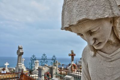 Close-up of female sculpture at cemetery against sky