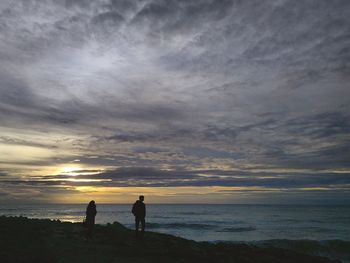 Silhouette men standing on beach against sky during sunset