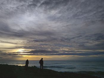 Silhouette men standing on beach against sky during sunset