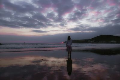 Rear view of woman standing at beach during sunset