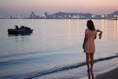 Rear view of woman standing on shore at beach against sky