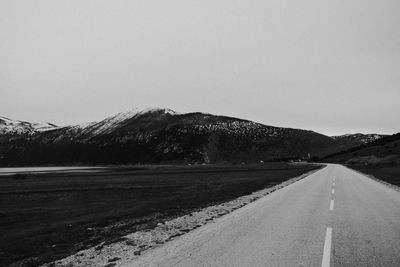 Road leading towards mountains against clear sky