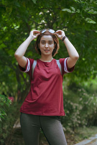 Portrait of young woman standing against trees