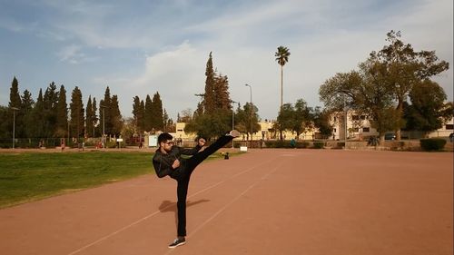 Man practicing karate kicking on field against sky