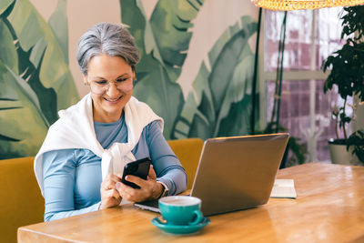 Young woman using mobile phone while sitting on table