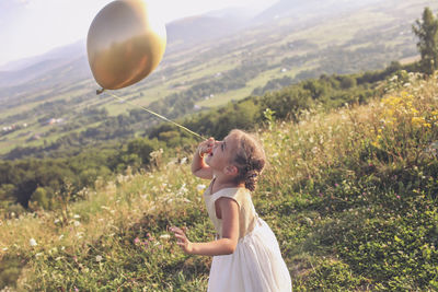 Side view of girl holding balloons on field