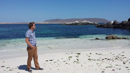 Full length of man with hands in pockets standing on shore at beach against sky